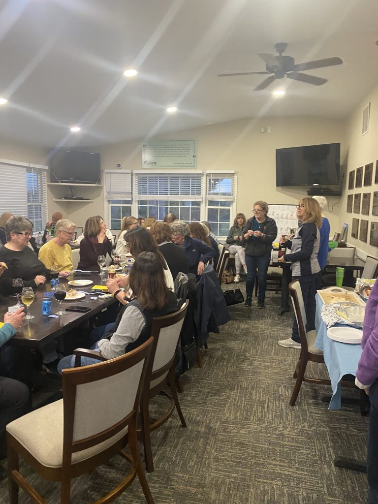 Women golfers holding a meeting at the clubhouse. A whiteboard is visible but its contents are blurry.