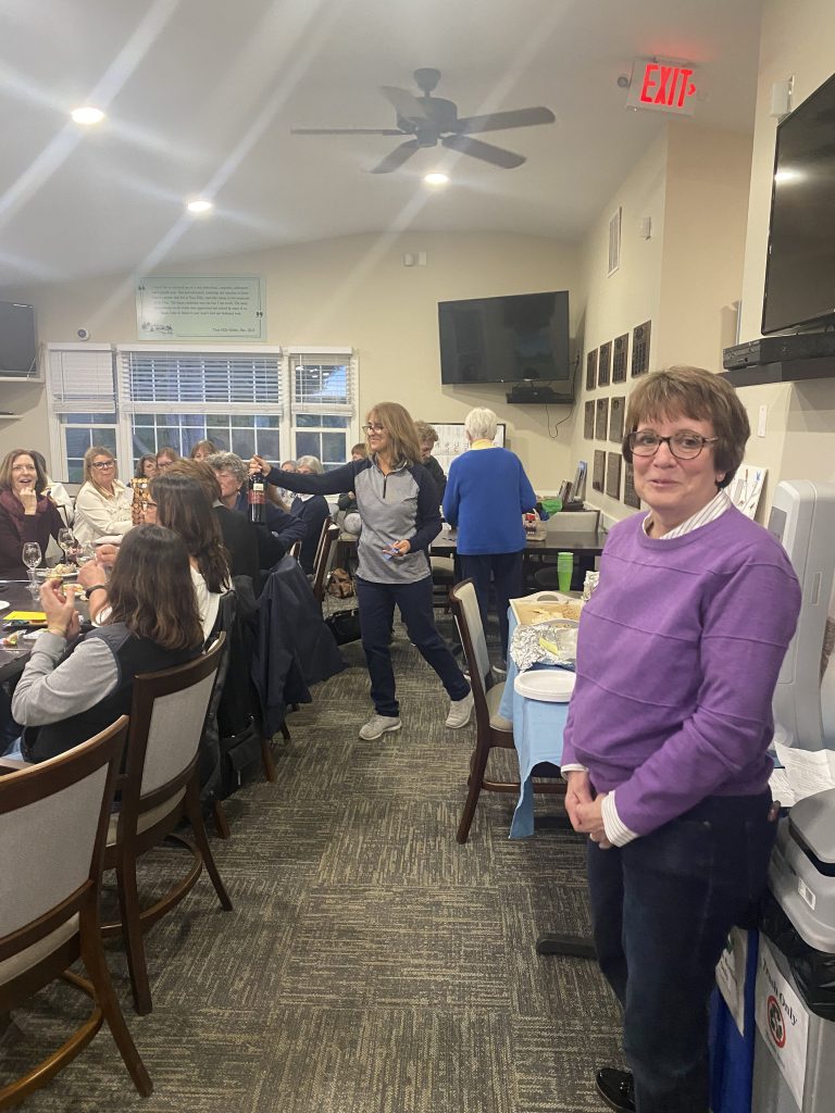 Women golfers holding a meeting at the clubhouse. A woman in a purple shirt stares at the camera.