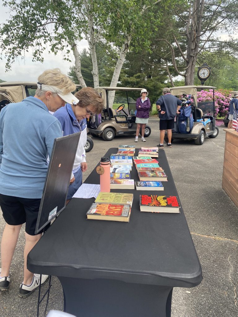 2 women take a look at a booth right outside the clubhouse. Various books are laid out on the table.